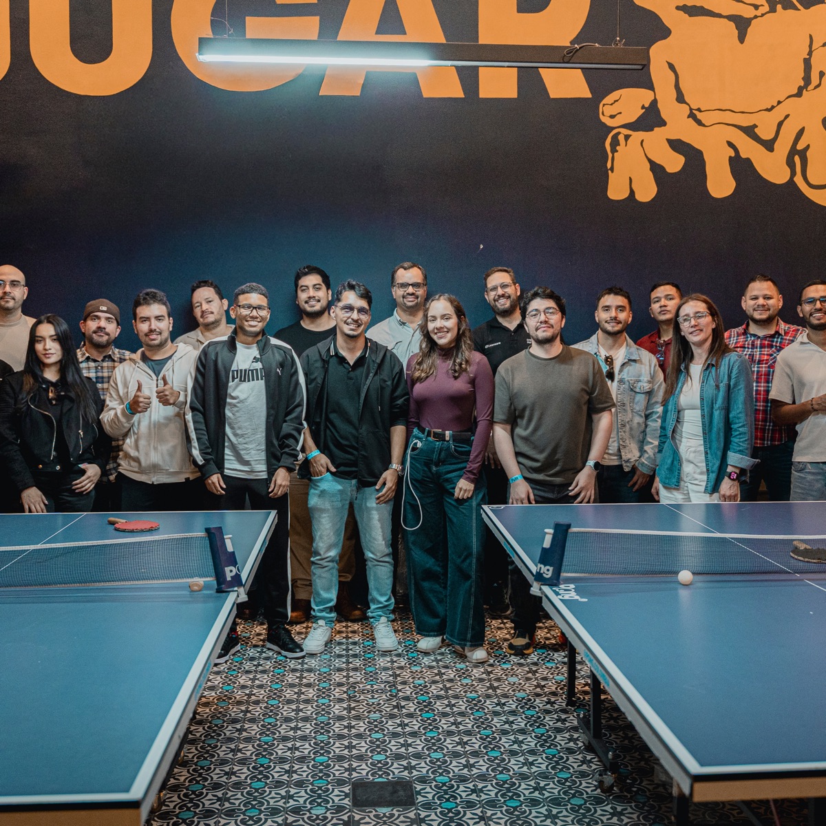 The Leanware team gathered between two ping-pong tables at a 2026 team event in Bogotá, Colombia, in front of a wall with a JUGAR sign